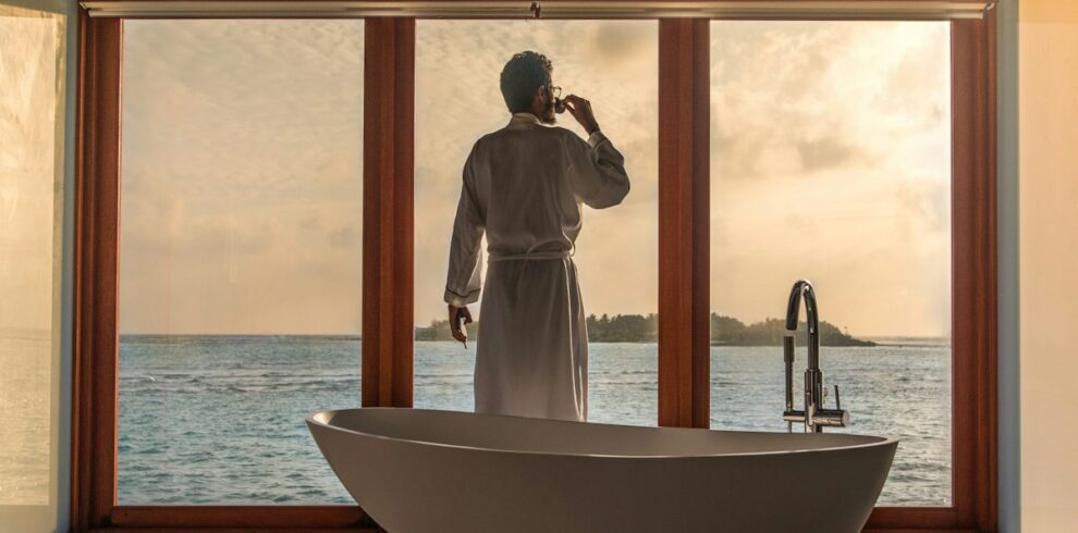 man standing in bathroom with bathtub next to body of water